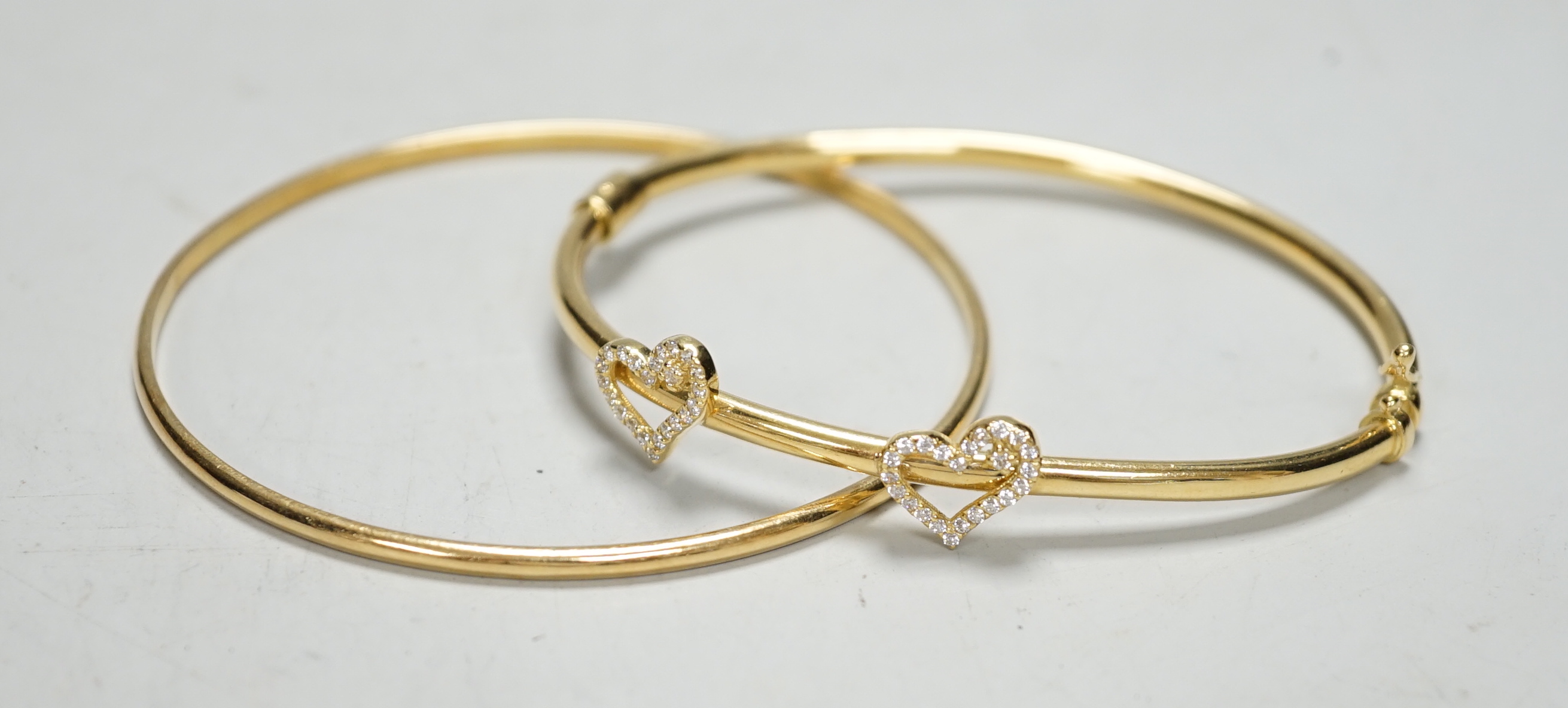 Two modern 750 yellow metal hinged bangles, one with diamond set twin hearts motif